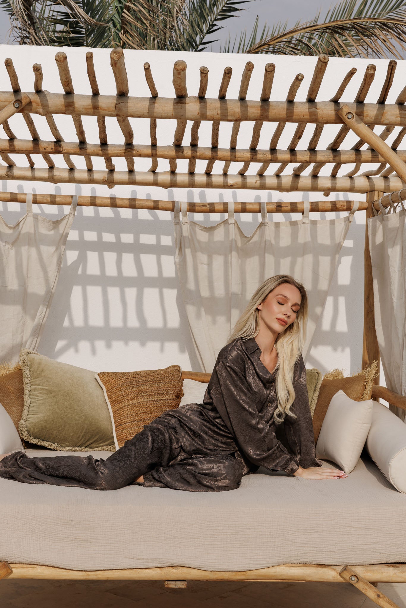 Luxury olive satin resortwear set with subtle animal print, featuring a relaxed shirt and wide-leg pants, styled on a sunbed with natural textures.