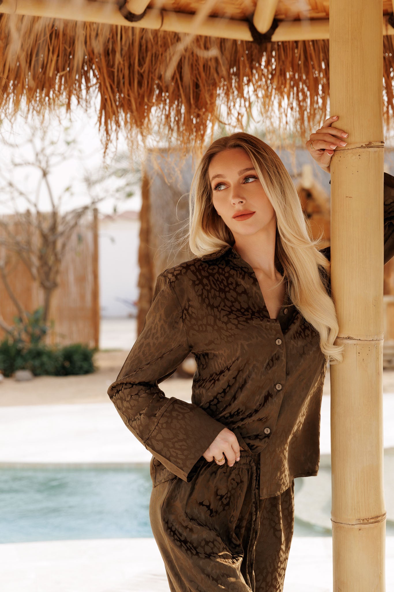 Luxury olive satin resortwear set with subtle animal print, relaxed button-up shirt and wide-leg trousers, designed for effortless vacation elegance.