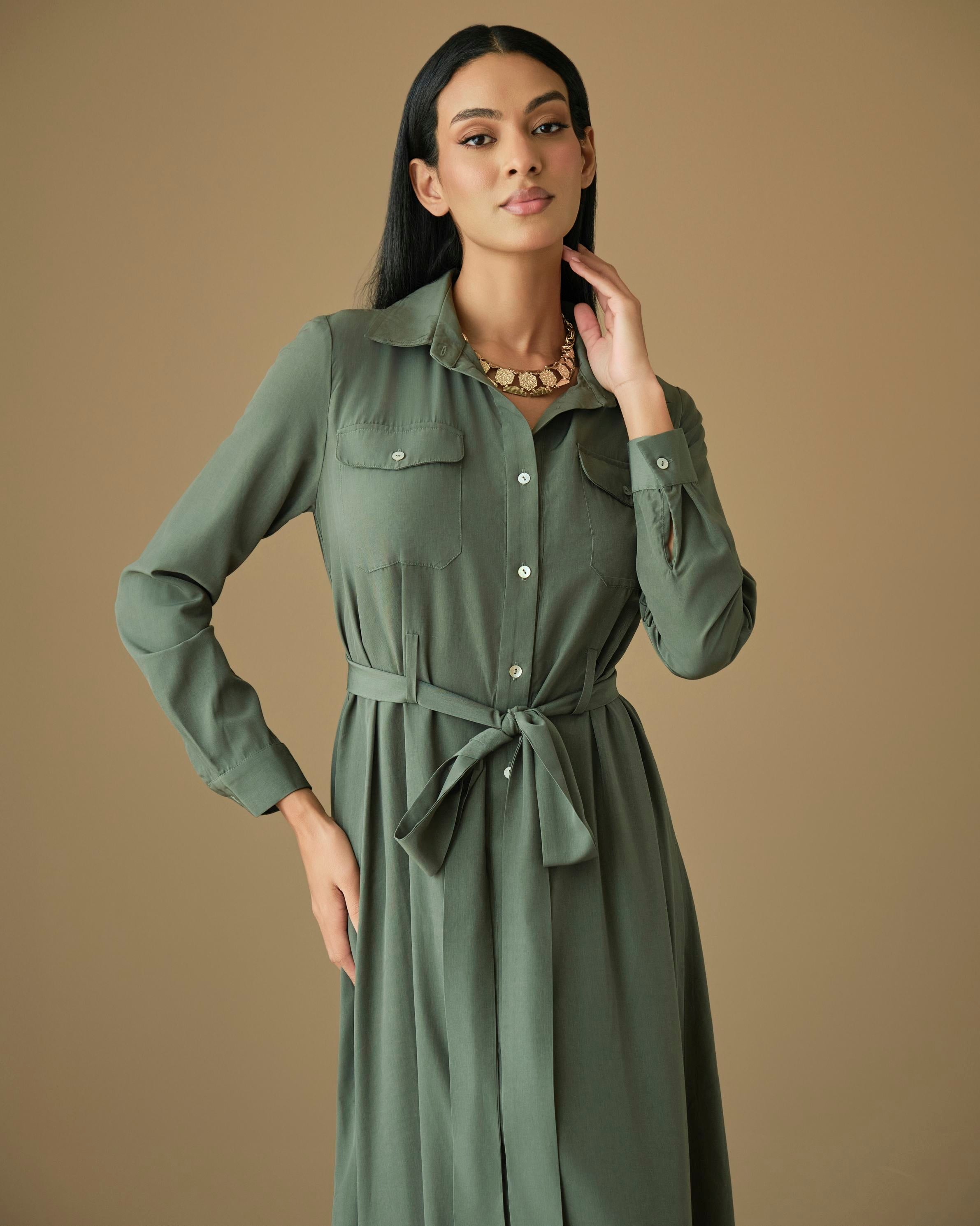 Close-up of a sage green shirt dress showing the collared neckline, button-front placket, flap chest pockets, and matching self-tie waist belt.
