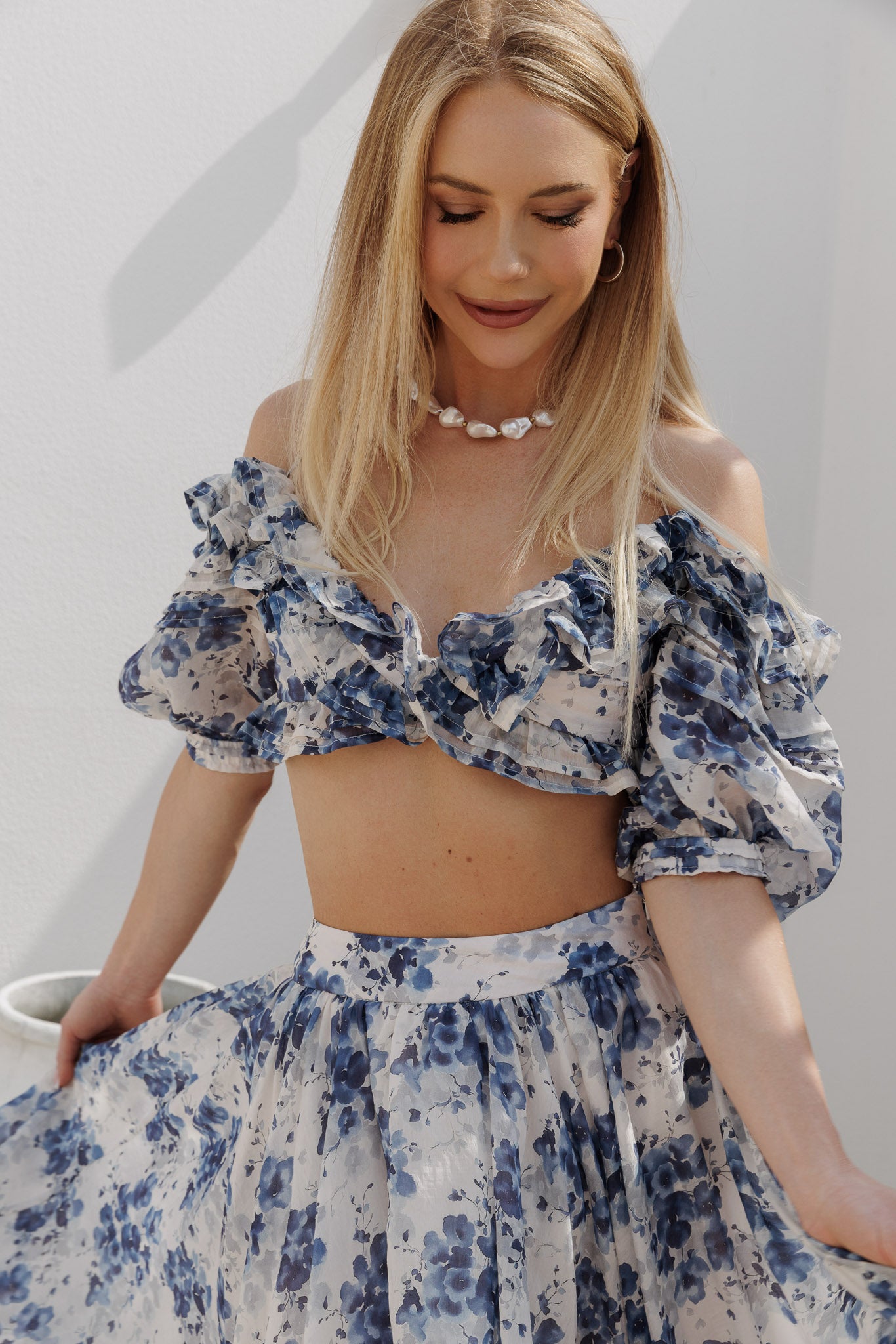 Blue floral two-piece set with an off-shoulder ruffled crop top featuring voluminous puff sleeves and a high-waisted gathered midi skirt with soft volume and flow.