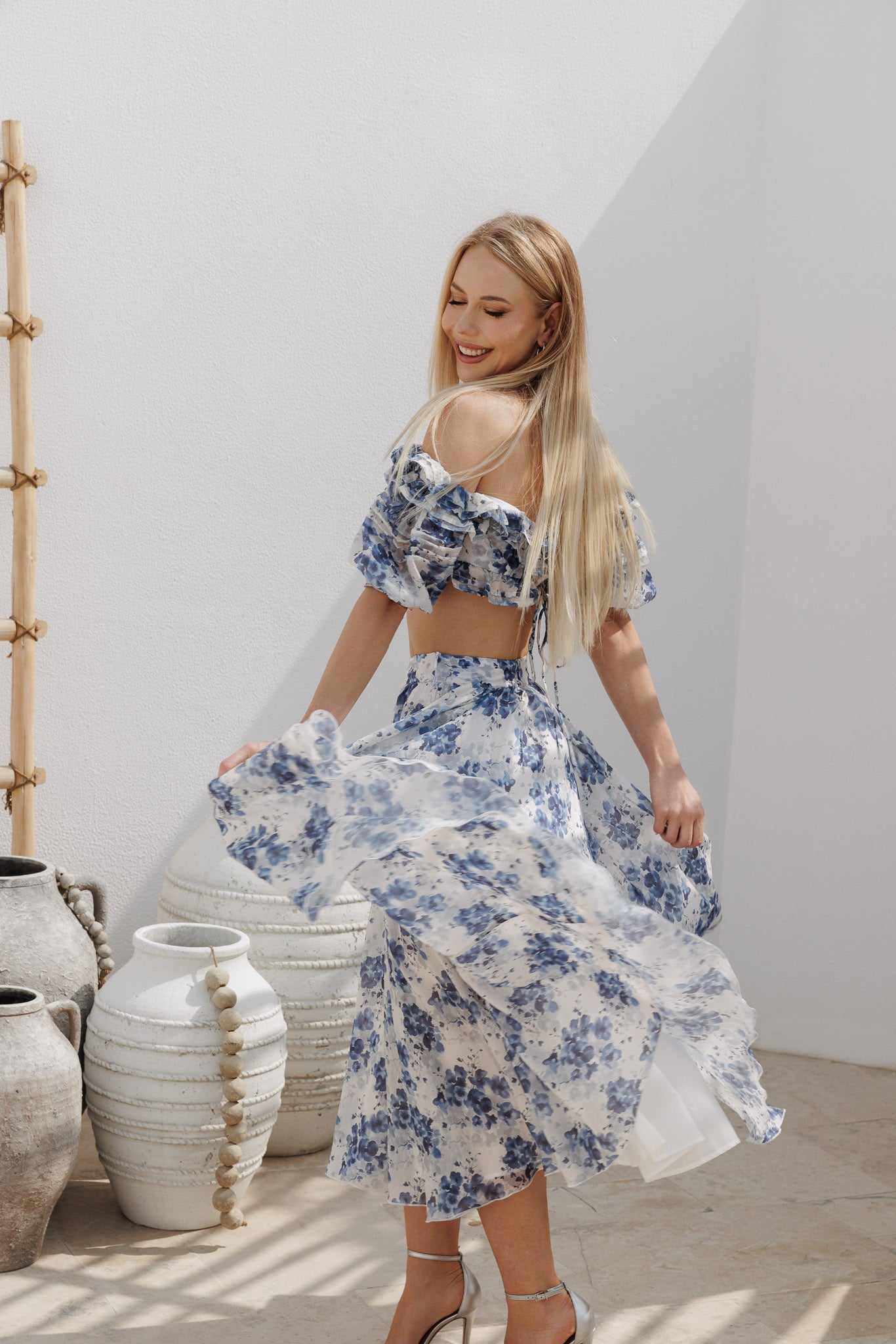 Blue floral two-piece set with an off-shoulder ruffled crop top featuring voluminous puff sleeves and a high-waisted gathered midi skirt with soft volume and flow.