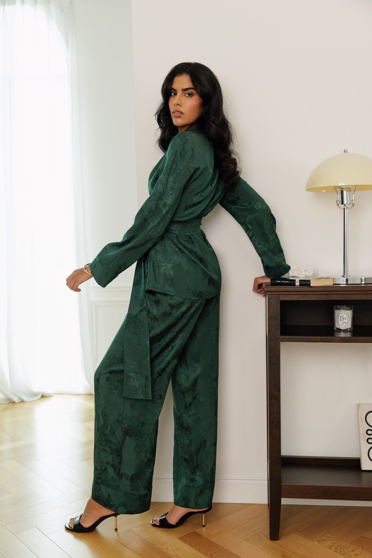 A woman modeling a dark green textured two-piece set consisting of a long-sleeve belted robe and matching wide-leg trousers.